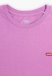 Fialové bavlněné tričko s žebrovaným kulatým výstřihem a malou červenou značkou Levi's na spodní levé straně. Hladká textura, jednoduchý design.