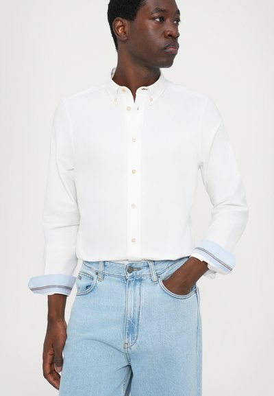 White button-up shirt with a classic collar, featuring light blue striped cuffs, worn with high-waisted light blue denim jeans.