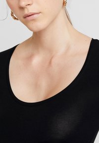 Crni bodi s okruglim izrezom napravljen od glatkog materijala; ima uski kroj i bešavne rubove. Zlate okrugle naušnice upotpunjuju izgled.