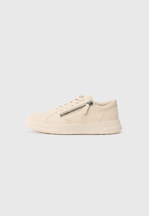 Sneaker bassa beige in pelle con lacci frontali, zip laterale, sole piatta e cuciture testurizzate su sfondo bianco.