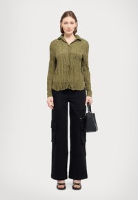 Olive green, textured long-sleeve shirt with a collar, paired with black cargo pants featuring multiple pockets and a straight-leg cut.