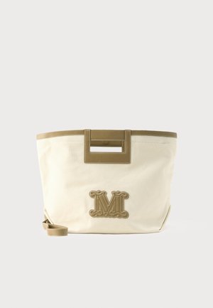 Beige canvas-totepose med brun læderkant, rektangulære udskårne håndtag, aftagelig rem og et dekorativt præget bogstav "M" foran.