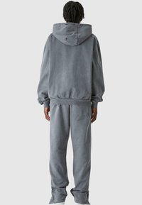 Szürke kapucnis pulóver és illeszkedő melegítőnadrág, melyek pamutból készültek. A pulóver nagy kapucnival és laza szabással rendelkezik, míg a nadrág oldalsó zsebet tartalmaz.