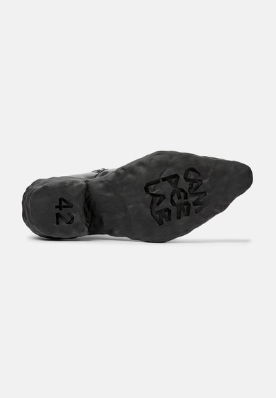 Suela de zapato negra con una superficie texturizada y rugosa, que presenta el número "42" en relieve y un patrón geométrico.