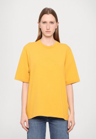 T-shirt en coton jaune avec un col rond et des manches courtes, présentant un logo en relief subtil sur le devant et une coupe décontractée.