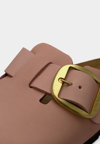 Λουρί δερμάτινου σανδάλου ανοιχτού καφέ με χρυσή πόρπη, σε κοντινή φωτογραφία που δείχνει υφή υλικού και λεπτομέρεια στερέωσης.