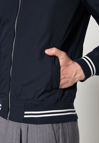 Chaqueta bomber azul marino hecha de un tejido ligero, con una cremallera plateada, puños de punto a rayas y bolsillos laterales.