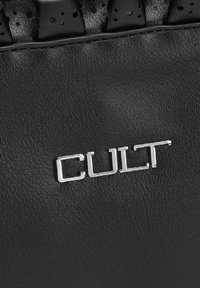 Il materiale in pelle nera presenta un logo metallico argentato "CULT". La superficie è liscia con una leggerissima texture, che arricchisce il design complessivo.