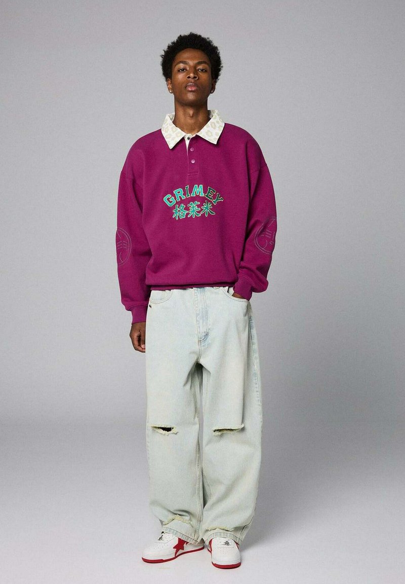 Felpa viola con logo "GRIMEY", colletto leggermente decorato, abbinata a pantaloni jeans oversize azzurri e scarpe bianche con accenti rossi.