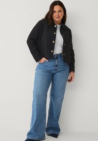 Black cropped jacket with gold buttons, paired with light blue wide-leg jeans. The fabric appears smooth, creating a structured silhouette.