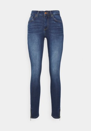 Jeans skinny em denim azul escuro, com uma cintura alta, cinco bolsos e fechos éclair no tornozelo para um detalhe adicional e ajuste de fit.