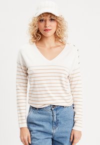 Langærmet V-hals sweater i creme med beige striber. Har knapdetaljer på skulderen. Sammen med højtaljede, lyseblå jeans.