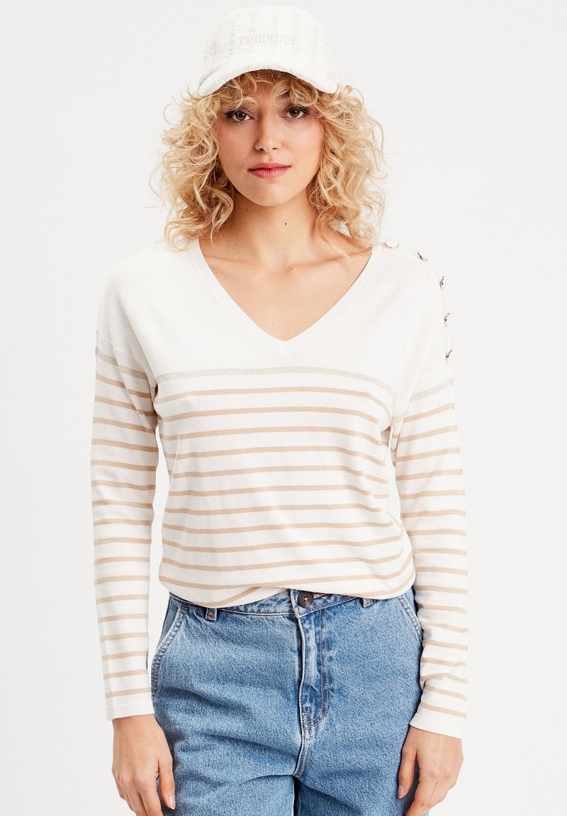 Langærmet V-hals sweater i creme med beige striber. Har knapdetaljer på skulderen. Sammen med højtaljede, lyseblå jeans.