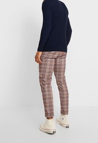 Navy ribbed knit sweater, brown plaid slim-fit trousers, and white high-top sneakers with black and red accents.