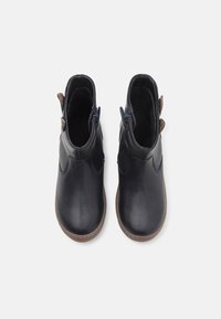 Botas de tobillo de piel negra con un acabado suave, que presentan una cremallera trasera y detalles texturizados en el talón. Suela de goma plana, con punta redondeada.