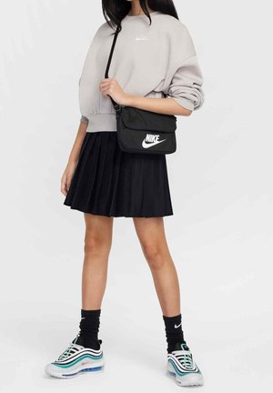 Sort plisseret nederdel, grå sweatshirt og sort Nike skuldertaske med logo. Hvide sneakers med grønne og pink detaljer. Strukturerede stoffer.