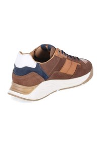 Zapatilla marrón con detalles en cuero marrón claro, parche en talón azul marino, suela blanca y cordones negros, inclinada para mostrar el lado exterior y la parte trasera.