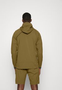 Olive green lightweight jacket with a hood, featuring a textured fabric and contrasting dark cuffs, paired with matching shorts.