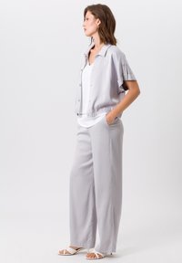 Veste cropped gris clair avec fermeture à bouton, pantalon ample assorti et top blanc. Texture lisse avec manches courtes et taille élastique.