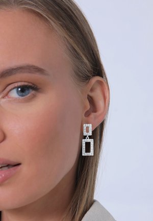 Hängende Ohrringe mit zwei gestapelten rechteckigen Formen aus silbernem Metall, verziert mit klaren Strasssteinen und einem eleganten Design.