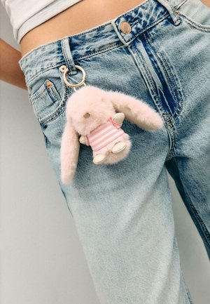 Petit porte-clés en peluche rose en forme de lapin, avec un t-shirt rayé, accroché à un passants de ceinture d'un jean en denim bleu clair.