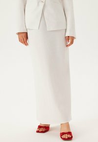 Vit skräddarsydd blazer, vit kjol, röda platta sandaler med en rosettdetalj. Slätt tyg, figursydd design, ankellång kjol.