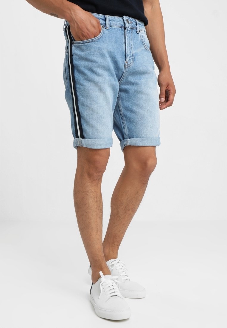Shorts en denim bleu clair avec un ourlet roulé et des rayures latérales noires. Dispose d'un design classique à cinq poches et d'un zip.