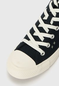 Svart canvas-sneaker med vita snören och ögla. Rund gummitåhätta, strukturerad sula och skyddande sömnadsdetalj.