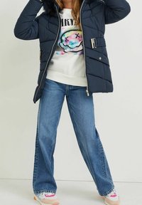 Chaqueta de plumón navy con capucha forrada de pelo, cintura ceñida con cinturón y cierre de cremallera, combinada con jeans de pierna ancha de color azul claro y zapatillas multicolor.
