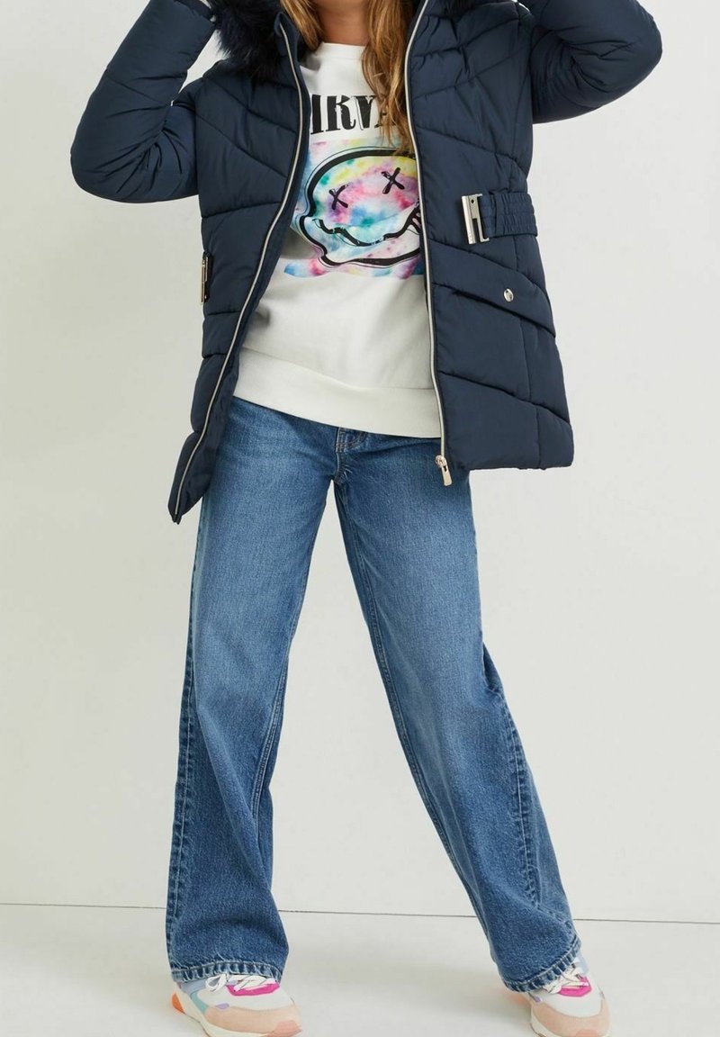 Chaqueta de plumón navy con capucha forrada de pelo, cintura ceñida con cinturón y cierre de cremallera, combinada con jeans de pierna ancha de color azul claro y zapatillas multicolor.