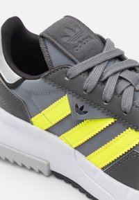 Šedé tenisky se neonově žlutými pruhy, texturovaný šedý a hladký černý svršek, polstrovaný jazyk a bílá mezipodešev s gumovou podrážkou.