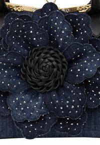 Jeans håndtaske har en mørkeblå blomst appliqué med lagdelte kronblade, fremhævet af rhinsten og et flettet sort center, hvilket forbedrer teksturen.