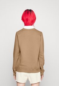 Brun sweatshirt med rundad halsringning, ribbade muddar och fåll, i kombination med ljusa shorts. Slät textur, avslappnad design.