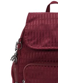 Zaino bordeaux con tessuto testurizzato e decorato, con coperchio pieghevole e hardware argentato, dotato di un portachiavi a cartone animato e una zip laterale.