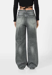 Vaqueros gris de pierna ancha con textura deslavada. Presentan dos bolsillos traseros y una cintura alta. Combinados con un top negro corto.
