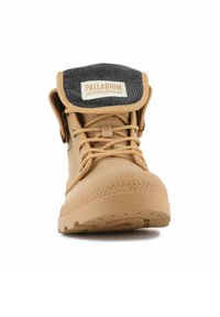 Bottine en caoutchouc beige avec une semelle texturée, un devant à lacets et un revers en velours côtelé gris replié arborant un logo à l'extérieur.