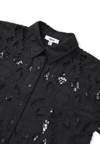 Blusa nera in pizzo con motivi floreali, chiusura con bottoni e colletto. Il materiale sembra leggero con una finitura testurizzata.