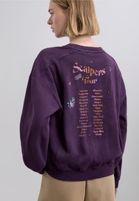 Lilla sweatshirt med løs pasform, med printet grafik med teksten "Scalpers Tour" og en liste over navne, tekstureret stof, ribbede ærmegab.