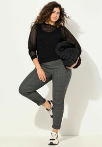 Svart nät långärmad topp lager ovanpå en grå rutiga skjorta, matchad med grå avsmalnande byxor och svarta sneakers med vita detaljer.