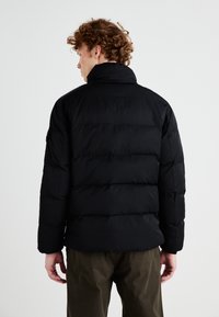 Svart puffjakke med quiltet design og stående krage. Har lange ermer og elastiske mansjetter, laget av glatt, lett materiale.