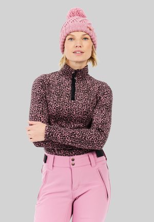 Kraagfleece met een zwart luipaardprint patroon, gecombineerd met roze broeken. Een dikke roze gebreide beanie met een pompon maakt de outfit compleet.