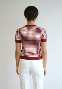 Czerwono-biały, krótki sweter z dzianiny z diamentowym wzorem, z prążkowanym dekoltem i krawędzią, zestawiony z białymi spodniami.