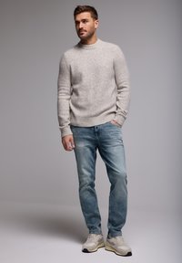 Maglione lavorato a maglia grigio chiaro con polsini a coste, abbinato a jeans blu sbiaditi e sneakers beige. Design semplice e rilassato con vestibilità classica.