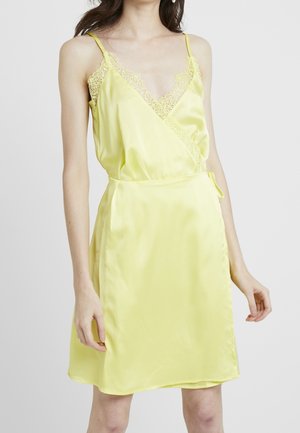 Sleeveless pale yellow satin dress with lace trim, wrap-style bodice, and tie detail at the waist, worn by a standing woman.
