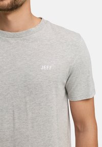 Lichtgrijs t-shirt met korte mouwen, gemaakt van zacht materiaal, met een klein wit geborduurd logo "JEFF" op de linker borst.