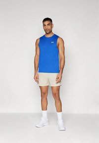 Sinine varrukateta sportlik särk koos logoga, paaritatud beežide lühikeste pükstega ning valgete tossudega. Modell seisab sirgelt ühevärvilise tausta ees.