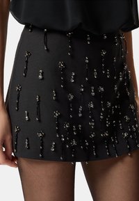 Mini gonna nera con tessuto testurizzato e decorazioni sparse di perline e cristalli di varie dimensioni e forme.