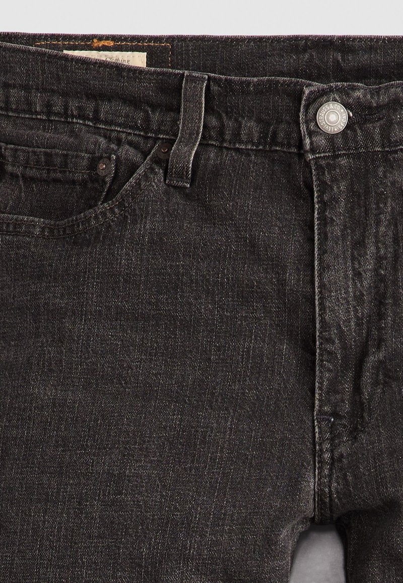 Jeans de mezclilla negra con un diseño clásico de cinco bolsillos, cierre de botón y una textura sutil. Incluye costuras visibles y una etiqueta.