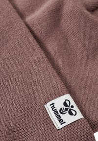 Tkanina polarowa w stonowanym kolorze mauve, z teksturowanym wykończeniem. Zawiera białą metkę z czarnym logo "hummel" i grafiką.