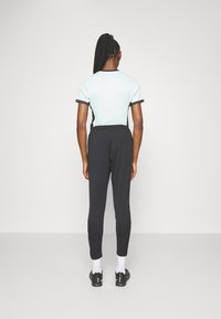 Camiseta de menta clara con ribetes negros, combinada con pantalones ajustados negros. El modelo está de espaldas a la cámara, vistiendo calcetines blancos y zapatos negros.